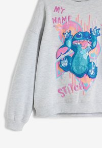 Grå sweatshirt med en glansig blå tecknad karaktär med utsträckta armar, omgiven av livfulla rosa och orangea grafiska detaljer.