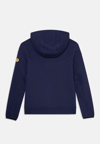 Un sweat à capuche bleu marine à manches longues, doté d'une capuche et d'un petit logo circulaire jaune sur la manche gauche, présenté de dos sur un fond blanc.