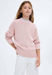 Ljust rosa stickad tröja med ribbad nederkant och mudd, försedd med rund hals och ett strukturerat mönster, tillsammans med vita byxor.