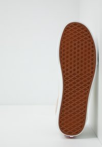 Suola di sneaker con un fondo in gomma marrone texturizzata, bordi bianchi e un accento rosso. Il design presenta un motivo geometrico per una migliore aderenza.