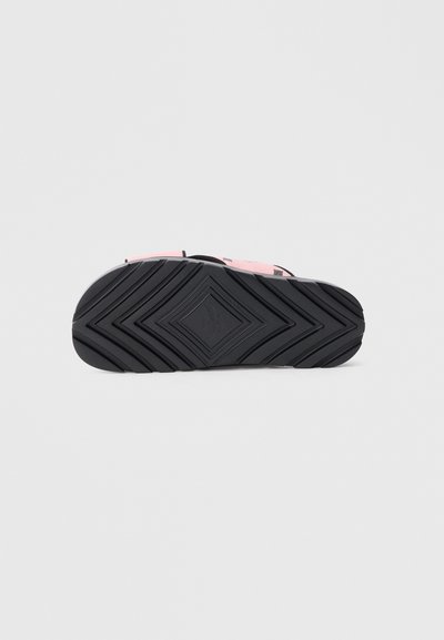 Sort gummisål med geometrisk mønster og markante riller; har en lyserød øvre del med sorte accenter.