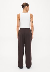Vitt ärmlöst bodysuit i kombination med högmidjade, bruna vida byxor. Byxorna har sidfickor och en mjuk textur.