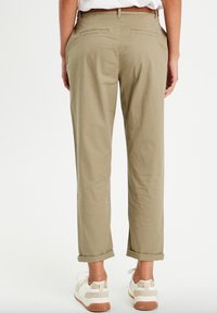 Chinos kaki à coupe droite, avec deux poches arrière, des poignets retroussés et un tissu lisse. Associés à des baskets blanches.