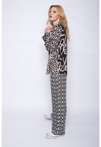 Schwarz-beige gemusterte Langarmbluse mit Leopardenmuster und geometrischen Designs, kombiniert mit passenden weiten Hosen. Dazu werden weiße Sneakers getragen.