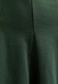 Zielony materiał z teksturowanym splotem, z subtelnym połyskiem. Tkanina układa się gładko, prezentując czysty, zorganizowany design.