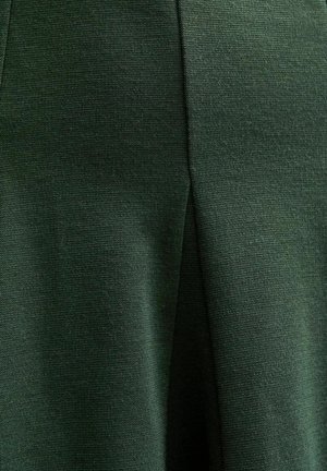 Tissu vert avec un tissage texturé, présentant un éclat subtil. Le matériau tombe en douceur, mettant en valeur un design épuré et structuré.