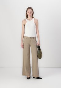 Beige kalhoty s širokými nohavicemi z bavlněné textilie, spárované s bílým žebrovaným tílkem. Modelka drží malou olivově zelenou kabelku. Černé špičaté baleríny.