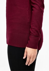 Bordowy sweter z prążkowanym dołem i mankietami, wykonany z miękkiego dzianinowego materiału. Widok z boku ukazujący dopasowany krój i gładką fakturę.