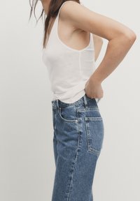 Vit åtsittande linne i kombination med högmidjade blå denimjeans. Jeansen har klassiska fickor och en något sliten tygtextur.