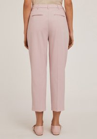 Pantalons ajustés rose clair avec une coupe droite, dotés de poches arrière et d'un ourlet soigné. Le matériau semble lisse et légèrement texturé.
