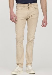 Jean slim beige en denim, avec un design classique à cinq poches, associés à des baskets blanches. Texture lisse avec un léger dégradé.