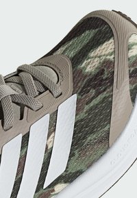 Zielono-brązowe buty sportowe w wzór kamuflażu z jasnobrązowymi sznurowadłami, białymi trzema paskami i białą podeszwą z logo Cloudfoam.
