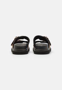 Black sandals featuring two straps, a flat sole, and metallic hardware accents. The texture is smooth with a slight sheen.
