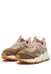 Pár hnědých a béžových tenisek s texturovanou kožešinou, zelenými semišovými akcenty, bílými tkaničkami a robustními gumovými podrážkami na bílém pozadí.