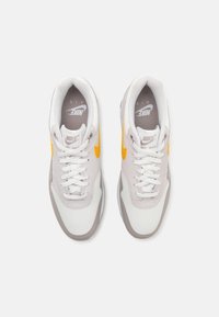 Nike Air Max sneakers med en hvid mesh overdel med grå accenter og en gul swoosh. Klassisk snørebåndsdesign og polstret krave.
