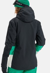 Schwarze Skijacke mit grünen und weißen Akzenten, Kapuze und verstellbaren Bündchen. Glattes, wasserabweisendes Material mit tailliertem Design.