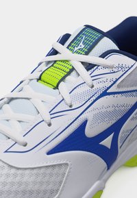 Λευκό και μπλε αθλητικό παπούτσι με λευκά κορδόνια, νεον πράσινες λεπτομέρειες και ύφασμα από δίχτυ στο επάνω μέρος.