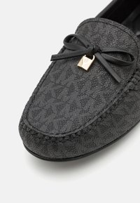 Sorte loafers lavet af tekstureret stof, der har en bånddetalje med en guldfarvet accent og dekorativt syning langs kanten.