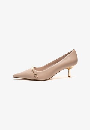 Stiletto beige con punta afilada, con una textura de cuero suave, que presenta un acento de cadena dorada y un pequeño tacón metálico.