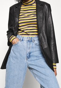 Svart läderblazer över en randig turtleneck i flera färger; högmidjade ljusblå jeans i lös passform. Ränderna inkluderar gult, lila och vitt.