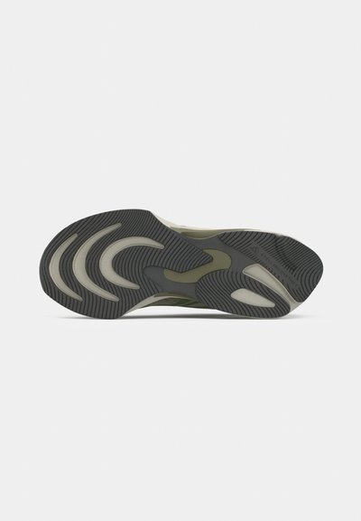 Suela de zapatilla deportiva verde y negra con surcos curvados y patrones de tread para tracción y flexibilidad.