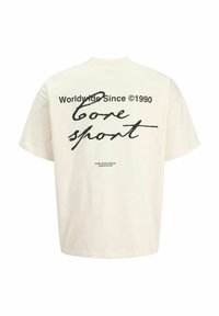 Krémovo biele tričko s krátkym rukávom s čiernym textom: „Worldwide Since ©1990 Core sport“ a menším nápisom „Core Sportswear Association“ na zadnej strane.