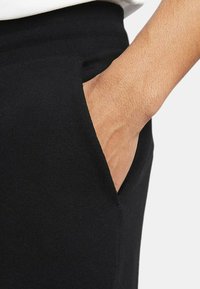 Pantaloni in maglia neri con tasca laterale. La vista ravvicinata mostra il tessuto testurizzato e una vita aderente, mettendo in risalto la forma e l'apertura della tasca.