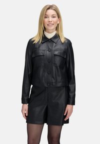 Zwarte leren cropped jack met een knoopsluiting aan de voorkant, puntige kraag en twee borstzakken, gecombineerd met zwarte leren shorts.