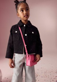 Svart texturerad jacka med silverknappar och fickor fram. Kombinerad med ljusgrå vida jeans och en liten rosa kviltad handväska.