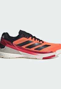 Oranžová a černá atletická bota s horní částí z prodyšné síťoviny, třemi černými pruhy, strukturovanou podrážkou a červenými akcenty po boční straně.