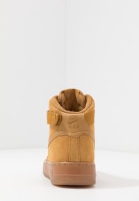 Höga Nike Air sneakers i brunt mocka med gummisula, sedda bakifrån mot en vit, hörnig bakgrund.