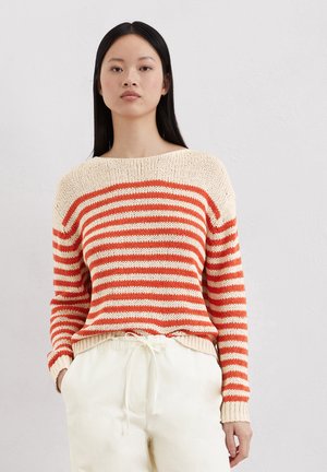 Gestrickter Pullover mit cremefarbenen und orangen Streifen, ausgestattet mit einem Bootsausschnitt und gerippten Bündchen. Kombiniert mit hellen Hosen.