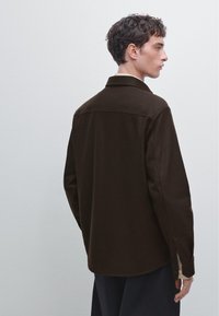 Bruine wolmix shirtjack met een gestructureerde kraag, knoopmanchetten en een rechte snit. De achterzijde benadrukt de gladde textuur en de zachte silhoët.
