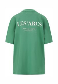 Grøn oversized t-shirt med rund halsudskæring. Har hvid tekst på ryggen: "LES' ARCS" og "NEW BAD HABITS" med en struktureret finish.