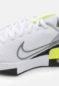 Hvide Nike sneakers med en mesh-overdel, grå swoosh og sorte detaljer. Har en lys gul hældetalje og flade hvide snørebånd.