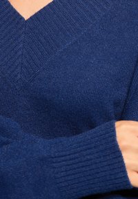 Dunkelblau gestrickter Pullover mit V-Ausschnitt, geripptem Muster und langen Ärmeln. Der Stoff wirkt weich und leicht strukturiert.