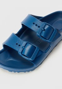 Niebieskie sandały z formowanego plastiku, wyposażone w dwie regulowane paski z kwadratowymi klamrami, teksturowaną wkładkę oraz wyprofilowaną podeszwę zapewniającą komfort.