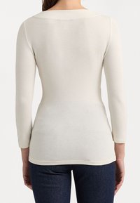 Cream-colored long-sleeve top with a smooth texture, rounded neckline, and a fitted shape, displayed from the back.
