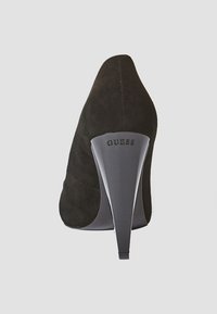 Černá semišová bota na vysokém podpatku s špičatou špičkou a elegantním, ostrým podpatkem. Na zadní straně podpatku je embosované logo "GUESS".