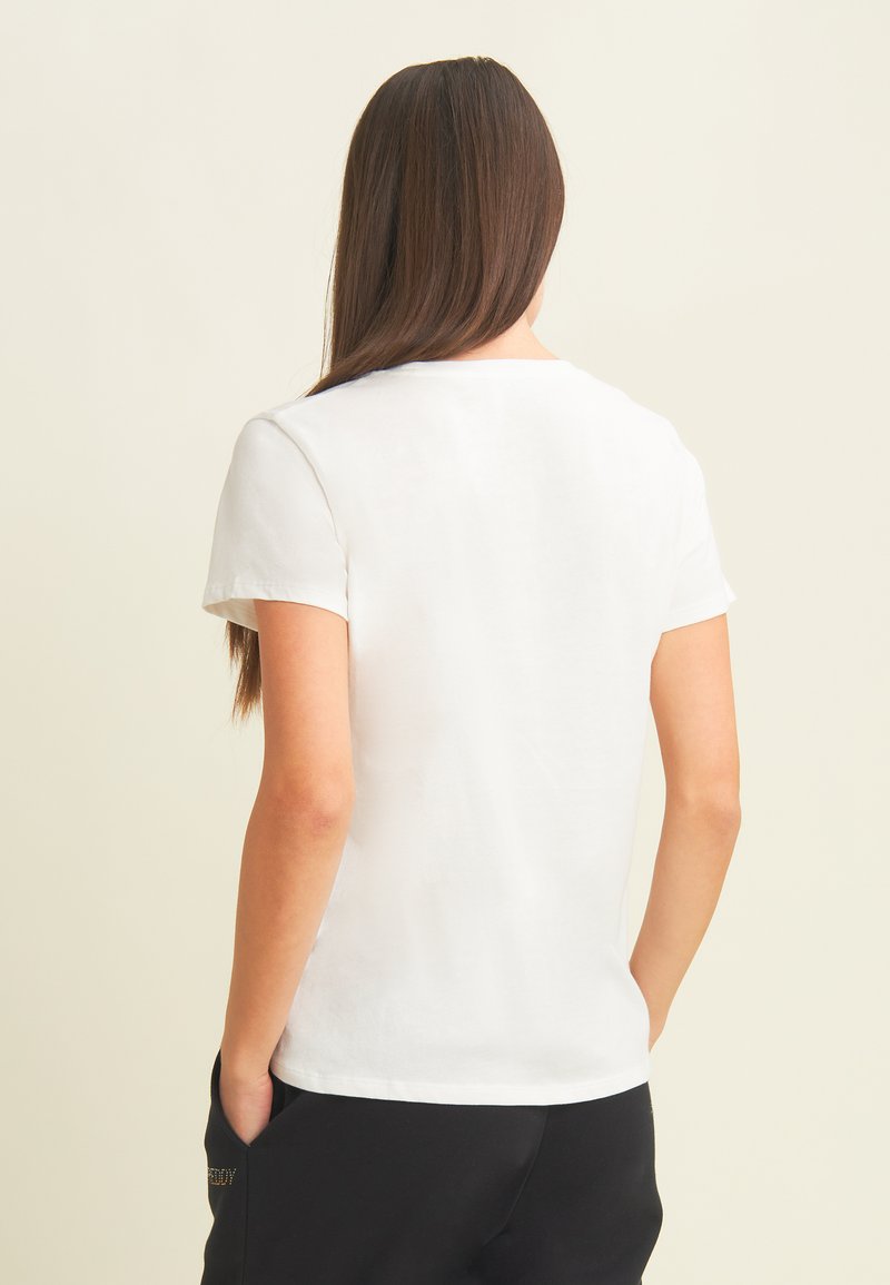 Camiseta blanca de manga corta hecha de tejido suave, con un clásico cuello redondo y una textura suave, combinada con pantalones negros.