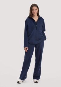Marineblauer Fleece-Pullover mit halbem Reißverschluss und Kängurutasche, kombiniert mit passenden weit geschnittenen Hosen. Glatte Textur, lockere Passform.