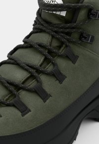 Green suede hiking boot featuring black laces, plastic eyelets, and a sturdy rubber sole. Textured panels and logo on the tongue.