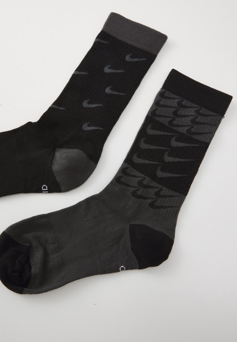 Zwei Paar schwarze Sportsocken. Das eine hat ein graues Logo-Muster; das andere zeichnet sich durch ein strukturiertes Design aus, beide mit verstärkter Ferse und Zehen.