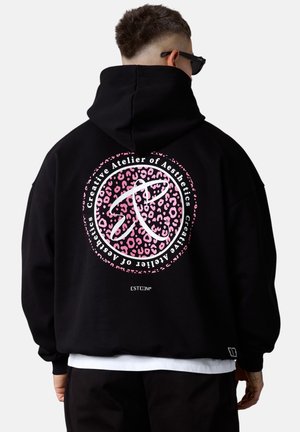 Haut à capuche noir oversize avec un motif circulaire en léopard rose et du texte blanc au dos. Fabriqué en tissu doux, avec une grande capuche.