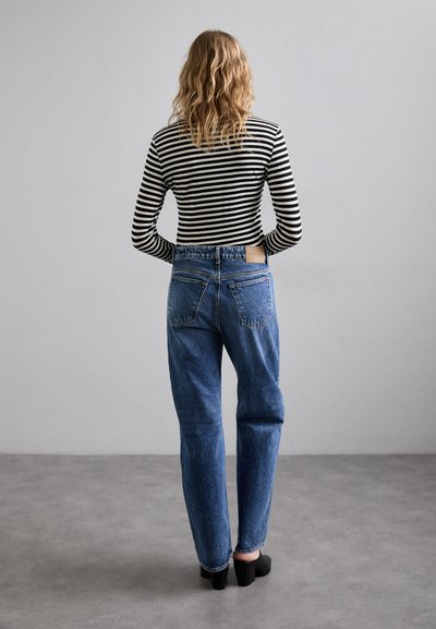 Högmidjade blå denimjeans med lös passform, tillsammans med en långärmad topp i svart och vitt randigt mönster, sedd bakifrån.