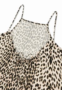 Camisole à imprimé léopard avec des bretelles spaghetti réglables, un décolleté à volants, un détail à nouer à l'avant, et un tissu lisse et léger.