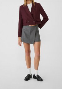 Bordeaux geknipte blazer met dubbele knopen, gecombineerd met een grijze streepdessin wikkelrok. Zwarte loafers en witte sokken maken de look compleet.