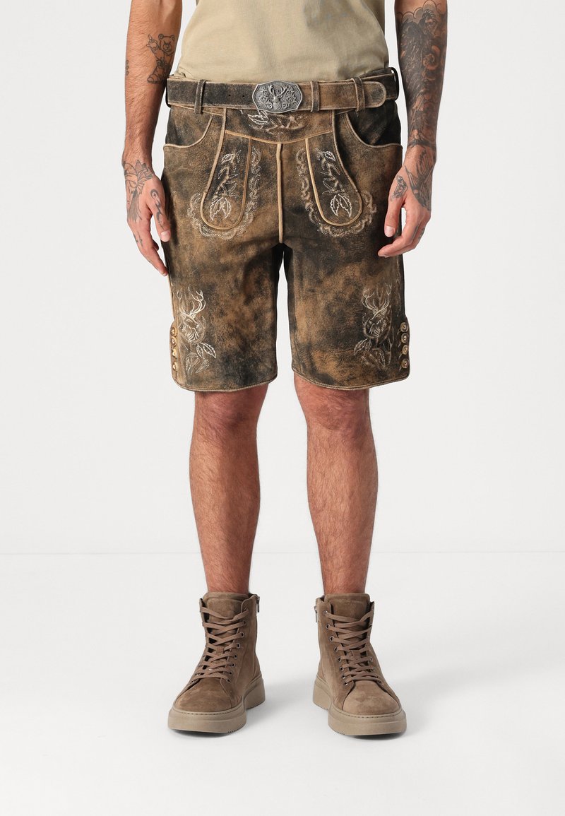 Brune lædershorts med detaljeret broderi, der har lommer og dekorative knapper på siden. Parret med brune høje sneakers.