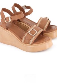 Sandalias de cuña marrones con dos tiras anchas, una de las cuales presenta acentos trenzados y una hebilla plateada. Parte superior de textura suave y suela de plataforma ligera.