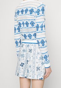 Niebieski i biały sweter z dzianiny z kwiatowym wzorem, teksturowanym splotem i niebieskimi wykończeniami. Połączony z dopasowaną spódnicą w podobne wzory i kolory.